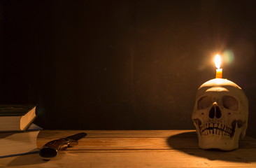 Human skull with candle light, Knife and book on wooden table in the dark background, Decorate for Halloween Theme with copy space.