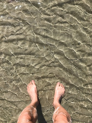 Person standing bare feet in the water at the beach