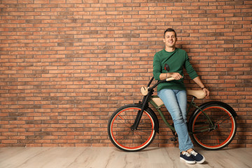 Canvas Print - Portrait of handsome young man with bicycle near brick wall