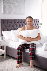 Wall Mural - Happy man with soft pillow sitting on bed at home