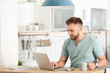 © New Africa - Young man using laptop at table in kitchen