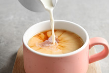 Pouring Milk Into Cup Of Black Tea On Gray Table, Closeup