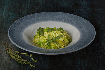 Dish of restaurant menu risotto with green asparagus and rucola on a beautiful dish on a green wooden background