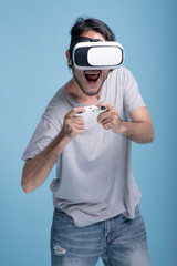 Wall Mural - Young bearded man playing VR game in blue background.