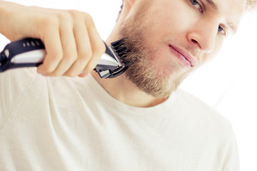 Wall Mural - isolated young hipster shaving beard with machine on white background