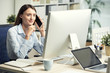 © DragonImages - Pretty young smiling business lady calling on phone and reading data on computer screen