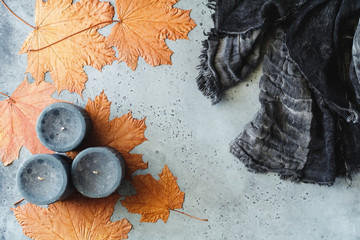 Wall Mural - Autumn flat lay composition on a grey concrete background. Maple leaves, black aromatic candles and warm scarf. Top view.