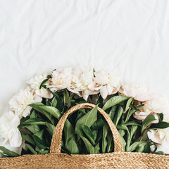 Wall Mural - Straw bag with white peony flowers on white background. Flat lay, top view summer floral concept.
