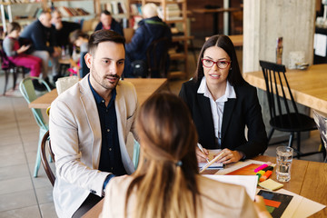 Wall Mural - Business meeting in coffee shop. Three young motivated colleagues discussing about new ideas and problems at work.