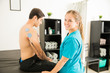 © AntonioDiaz - Smiling Physical Therapist Standing By Male Customer Receiving Electrotherapy