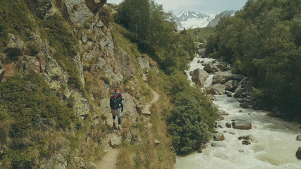 Wall Mural - mountain tourist walking along rapid river back view. hiking mountain