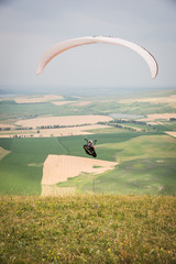 White orange paraglide with a paraglider in a cocoon against the background of fields of the sky and clouds. Paragliding Sports