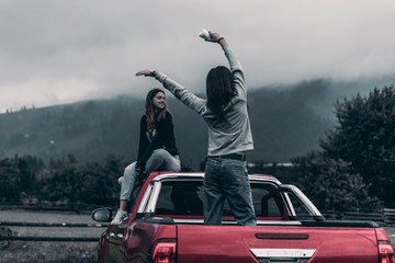 two girls sitting on the car and enjoy the view of the mountains and drink coffee. Concept Travel.