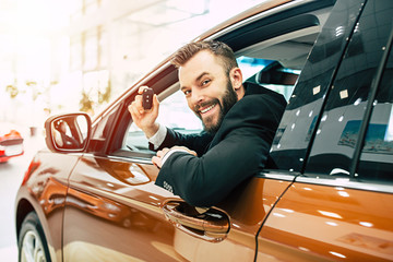 Happy buyer sitting in new car with keys in hand and looking on camera