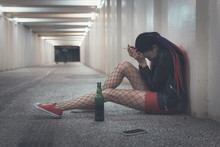 Woman Feel Depression And Alcoholism. Young Drunk Girl Sitting With A Bottle Of Whiskey In The Underpass Or Tunnels. Girl Is Experiencing Grief And Drinking Alcohol. Loneliness, Solitude, Desolation,