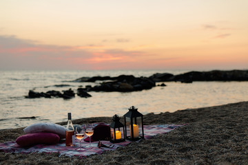 Wall Mural - Summer sea sunset. Romantic picnic on the beach. Bottle of wine, glasses, candles, plaid and pillows.