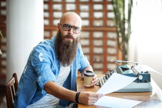 Bearded stylish writer with cup of coffe reading his novel