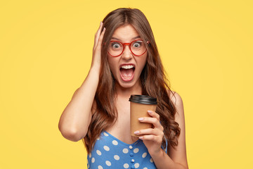 Wall Mural - Unsound angry student shouts at her boyfriend during coffee break, holds paper disposable cup with beverage, keeps jaw dropped, exclaims in irritation, dressed in polka dot blouse. Negative feeling