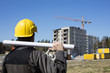 © Jarkko - Construction worker in dirty overalls and a yellow helmet in Finland. In his hand he has drawings. In the background is out of focus in the construction site.