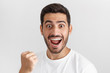 © Damir Khabirov - Young handsome man in blank white t shirt, shouting while his team win, raised fist in victory gesture, isolated on gray background