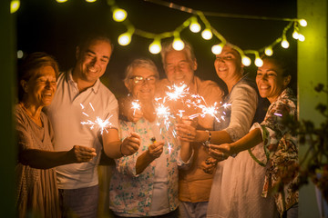 Wall Mural - group of people celebrate an event like new years eve or birthday all together with sparkles light by night in the dark. smiles and having fun in friendship for different ages men and women at home. 