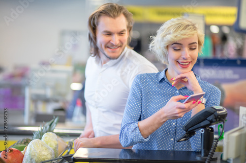 Fotografía Young couple bying goods in city mall, blonde pretty woman shows her coupons at