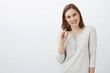 © Cookie Studio - Cute coworker have and eye on charming guy flirting during break biting frames holding eyewear in hand smiling tenderly at camera posing against gray background in casual white blouse