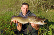 © sablin - Scène de pêche en eau douce. Pêcheur de carnassier tenant un gros brochet pris au leurre dans un petit étang