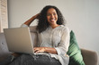 © Anatoliy Karlyuk - Indoor shot of positive charming young African American woman dressed in stylish clothes relaxing on sofa with portable computer on her lap, shopping online, looking away with cute cheerful smile