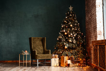 New Year Background. Christmas Room Interior Of Loft. Light, Gifts, Candles And Hot Lighting Indoors. An Armchair With A Table Near A Christmas Tree With Gifts