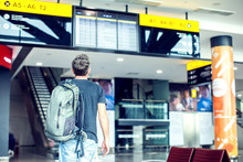 A Young Male Traveler With A Backpack Looks At The Information Board At The Airport. Getting Information About The Flight.