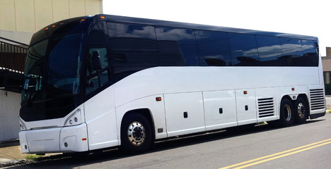 Charter tour bus parked  on urban street with nondescript buildings and white sky.