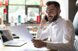 © Seventyfour - Portrait of handsome bearded businessman wearing white shirt speaking by phone and reading documents while working at table in office or cafe