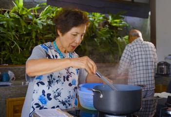 senior happy and beautiful retired Asian Japanese couple cooking together at home kitchen enjoying preparing meal relaxed in aged husband and wife love