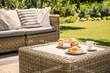 Beige color wicker table and settee on a porch during sunny afternoon in the garden. Croissants and coffee served on the table.