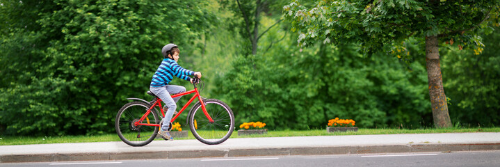 child on a bicycle at asphalt road in summer. Bike in the park. Boy cycling outdoors on beautiful sunny evening