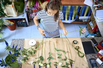 Wall Mural - Young florist cutting flower for bouquet at the counter of her shop