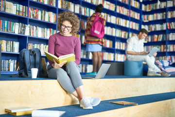 Young female student study in the university campus library, she is sitting and reading a book