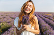 Photo of smiling brunette woman in dress holding bouquet with flowers, while walking outdoor through lavender field in summer