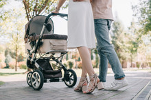 Cropped Image Of Parents Walking With Baby Carriage In Park