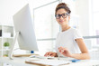© pressmaster - Young confident manager or designer sitting by her workplace in office in front of computer monitor