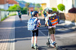 © Irina Schmidt - Two school kid boys in safety helmet riding with scooter in the city with backpack on sunny day. Happy children in colorful clothes biking on way to school.