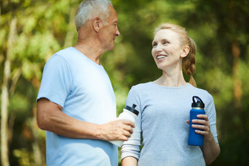 Wall Mural - Healthy mature man and woman in activewear having refreshment after workout in natural environment