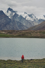 Wall Mural - traveller man in red jacket standing on meadow with lake and snow mountain view. travel lifestyle, a