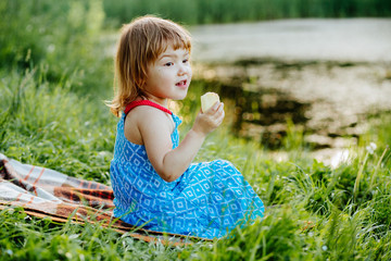 Cute blonde little baby girl sitting on the green grass in summer sunset.