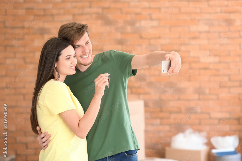 Young happy couple taking selfie with key of their new house indoors