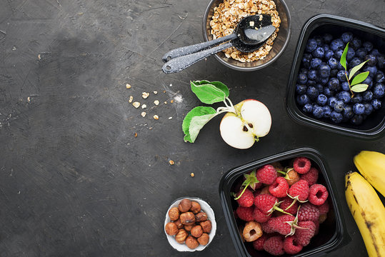 Black plastic containers take-away for a healthy snack food with raspberries, blueberries. Ingredients of healthy breakfast: granola, oat flakes, berries, nuts, apples, bananas. Top View.