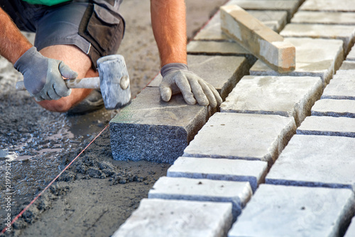 Fotografía A workman's gloved hands use a hammer to place stone pavers