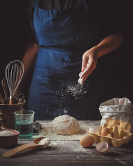 A young woman cooking homemade dough on a dark wooden rustic table. Toned image.