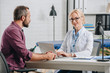 © LIGHTFIELD STUDIOS - smiling female physiotherapist typing on laptop during appointment with patient in hospital